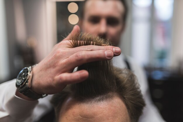 Unscharfer Friseur, der sich vorbereitet, Haar des Mannes zu schneiden
