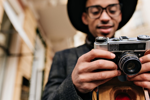 Unscharfes Porträt des konzentrierten afrikanischen Fotografen lokalisiert auf Stadtstraße. Außenfoto des stilvollen schwarzen Mannes mit der Kamera im Fokus.