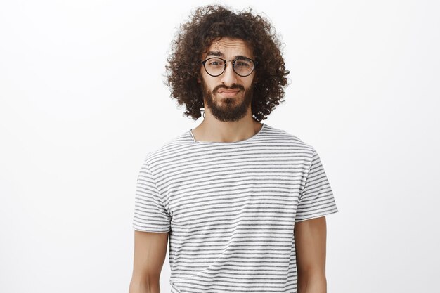 unsicherer gutaussehender bärtiger Mann mit lockigem Haar in trendiger schwarzer Brille, hochgezogener Augenbraue und zweifelndem Blick