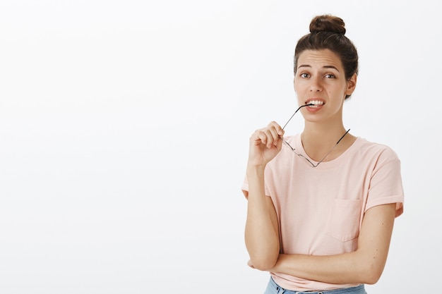 Unsicheres Mädchen mit Brille, die gegen die weiße Wand aufwirft