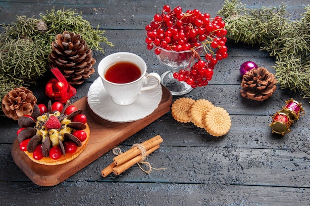 Unten Ansicht eine Tasse Tee und Beerenkuchen auf hölzernem Servierteller Johannisbeere in einem Glas Tannenzapfen Weihnachtsspielzeug Tannenbaumblätter auf dunklem Holztisch