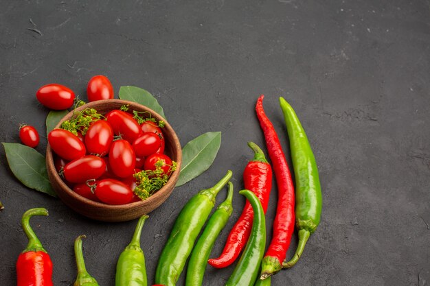 Unten sehen Sie eine Schüssel Kirschtomaten mit heißen roten und grünen Paprikaschoten und Lorbeerblättern auf schwarzem Hintergrund