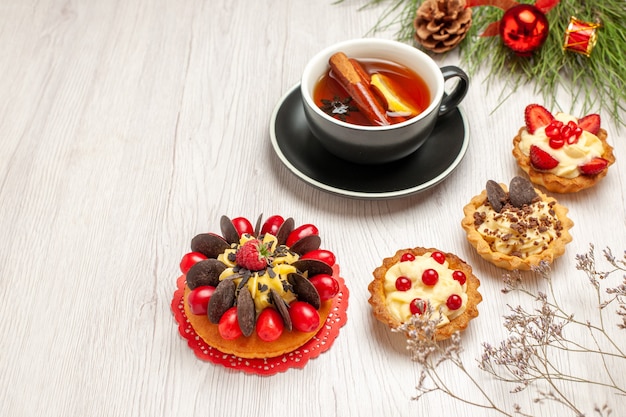 Unten sehen sie eine tasse zitronenzimt-tee-beeren-kuchen-törtchen und die kieferblätter mit weihnachtsspielzeug auf dem weißen hölzernen hintergrund