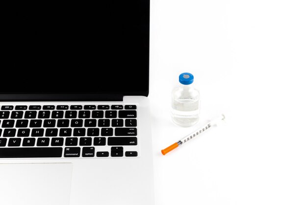 Unter quarantäne gestellter arbeitsplatz mit einem computer, einer spritze und einem impfstoff als symbol der impfung zum schutz der menschen. auf weißem hintergrund