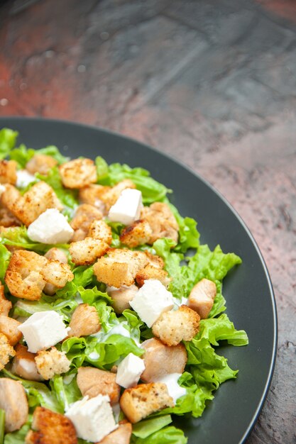 Unteransicht Caesar-Salat auf ovalem Teller auf dunkelrotem Tisch