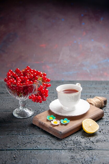 Untere Ansicht rote Johannisbeere in einem Glas eine Tasse Tee auf einer Schneidebrettscheibe Zitrone auf dunklem Hintergrund