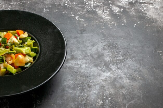 Untere Hälfte Ansicht grüner Tomatensalat auf ovalem Teller auf dunklem Freiraum