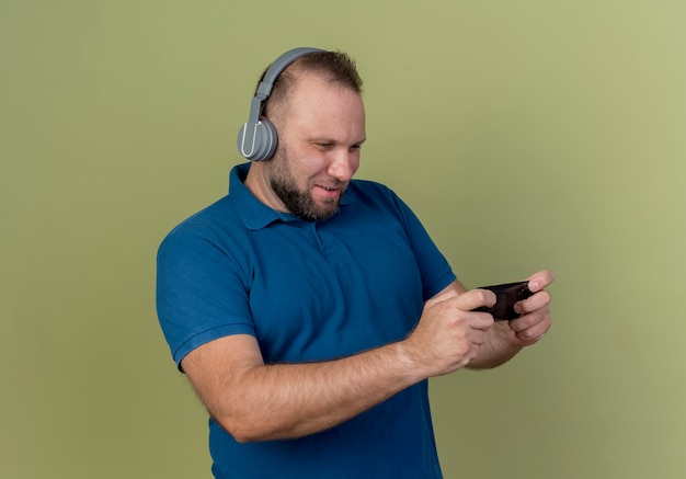 Unterhaltener erwachsener slawischer Mann, der Kopfhörer mit Handy trägt