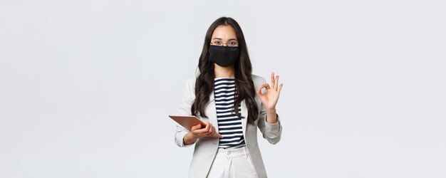 Unternehmensfinanzierung und Beschäftigung covid19 verhindert Virus und soziales Distanzierungskonzept Asiatische Geschäftsfrau mit digitalem Tablet trägt eine Schutzmaske gegen Viren und zeigt ein Okay-Zeichen