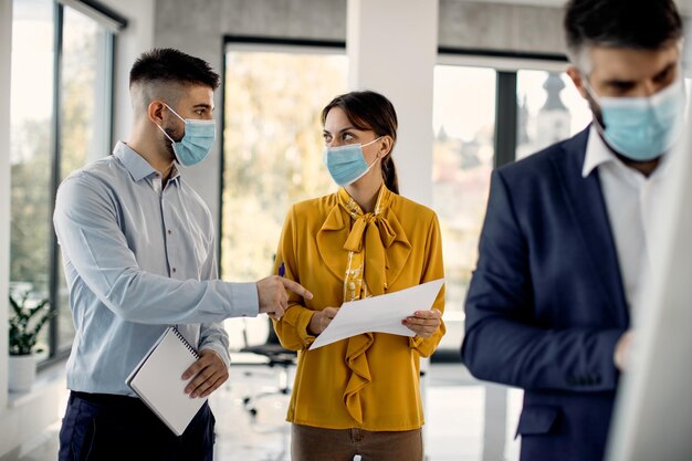 Unternehmer mit Gesichtsmasken, die während der Arbeit im Büro über Geschäftsberichte sprechen