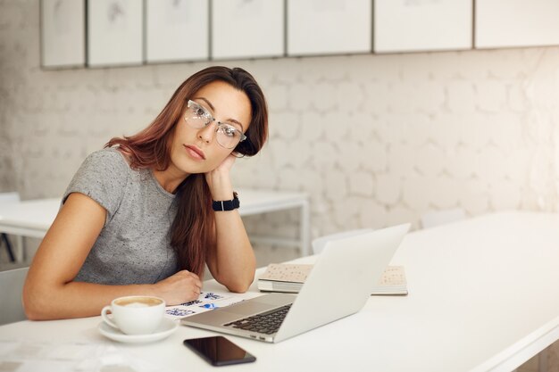 Unternehmerin, die einen erfolgreichen Online-Shop mit Laptop mit Brille in einem geräumigen Studio oder Café betreibt. Freiberufliches Konzept.