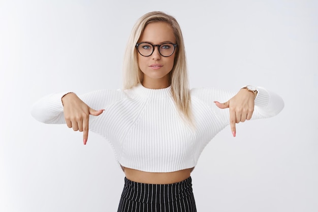 Kostenloses Foto unternehmerin in brille und mode-outfit, die nach unten zeigt und in die kamera schaut, was auf weiß hindeutet