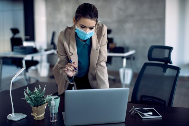 Unternehmerin mit Gesichtsmaske mit Laptop während der Arbeit im Büro