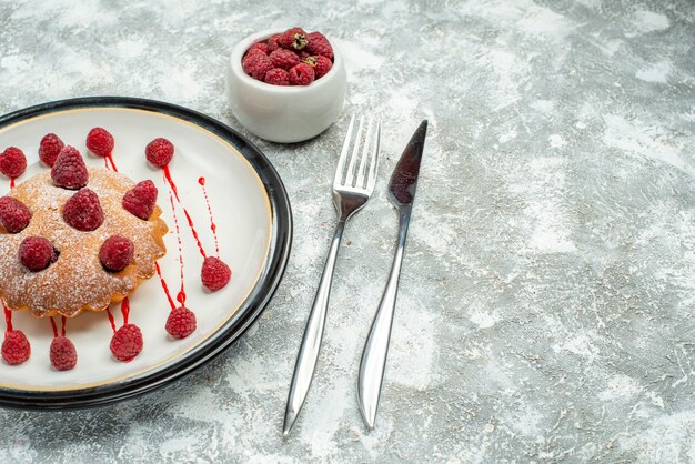 Untersicht Beerenkuchen auf ovalen Teller Himbeeren in Schüsselgabel und Tafelmesser auf grauem Oberflächenfreiraum