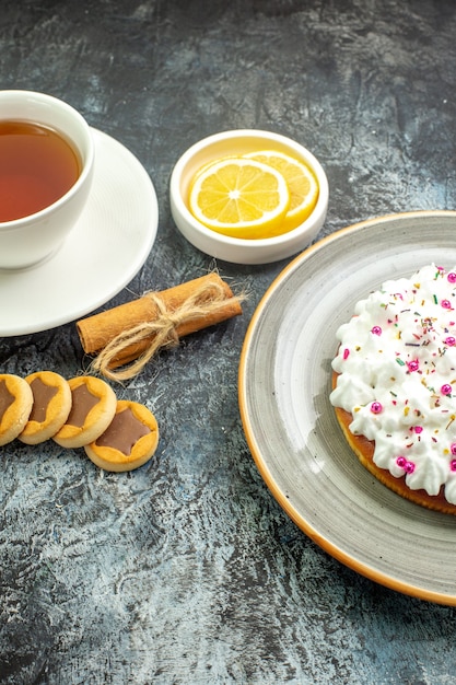 Untersicht Tasse Tee aromatisiert mit Zimt Zitronenscheiben in kleinen Untertassen Kekse Zimtstangen auf dunklem Boden