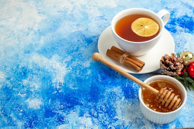 Untersicht Tasse Tee mit Zimt-Honig-Stick und Honig in Schüssel auf blauem Tisch