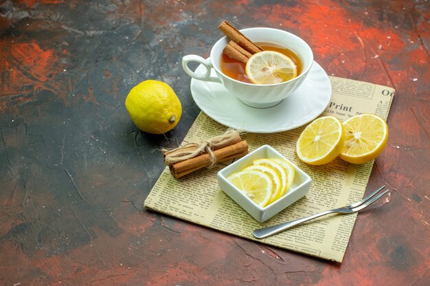 Untersicht Tasse Tee mit Zimt-Zitronen-Scheiben in kleiner Schüssel Gabel Zimtstangen mit Seil auf Zeitung auf dunkelrotem Tisch freier Raum gebunden