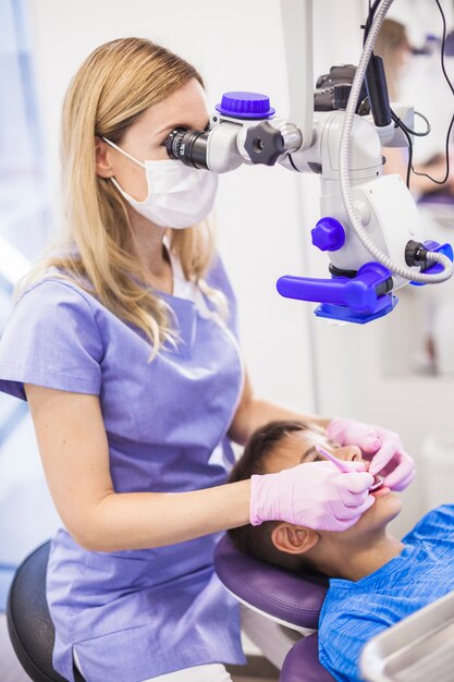 Untersuchungszähne des weiblichen Zahnarztes eines Jungen mit Mikroskop in der Klinik