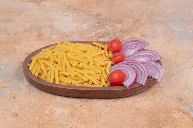 Unvorbereitete frische Makkaroni mit Zwiebelscheiben und Tomatenkirschen. Hochwertiges Foto