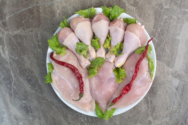 Kostenloses Foto unvorbereitete hähnchenschenkel mit pfeffer und salat auf weißem teller. foto in hoher qualität