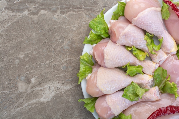 Unvorbereitete hähnchenschenkel mit salat auf weißem teller