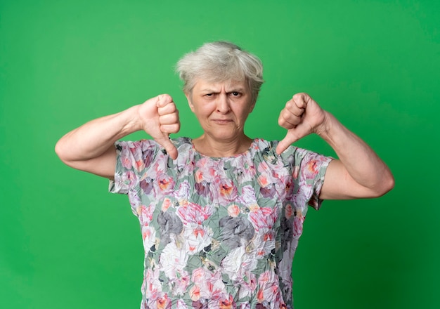 Unzufriedene ältere Frau Daumen nach unten mit zwei Händen isoliert auf grüner Wand