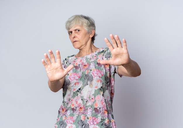 Unzufriedene ältere Frau verteidigt das Ausstrecken von Händen, die auf weißer Wand isoliert werden