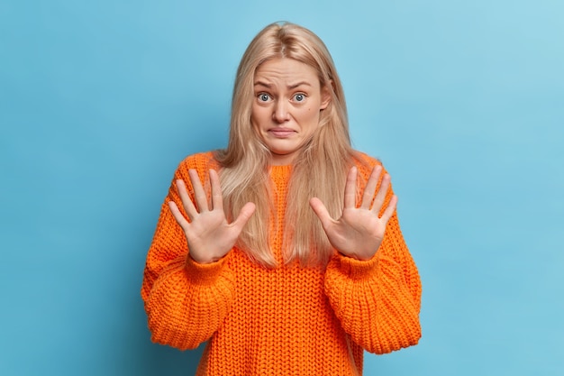 Kostenloses Foto unzufriedene blonde europäerin hebt die handflächen in ablehnung und stop-geste lehnt widerliches angebot ab smirks gesicht gekleidet in orange gestrickten pullover