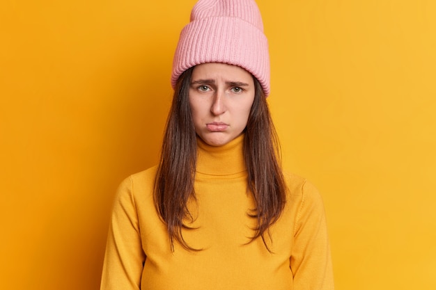 unzufriedene brünette junge Frau hat beleidigten Ausdruck mürrischer Blick drückt negative Emotionen aus trägt Hut und lässigen Pullover.