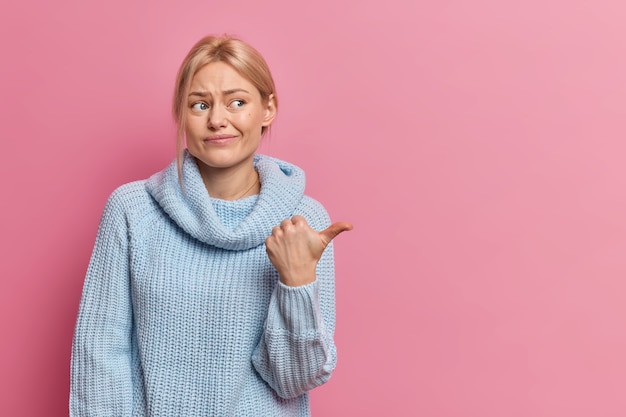 unzufriedene europäische Frau zeigt Daumen weg auf Kopierraum hat schlechte Gefühle Stirnrunzeln Gesicht trägt lässigen Pullover