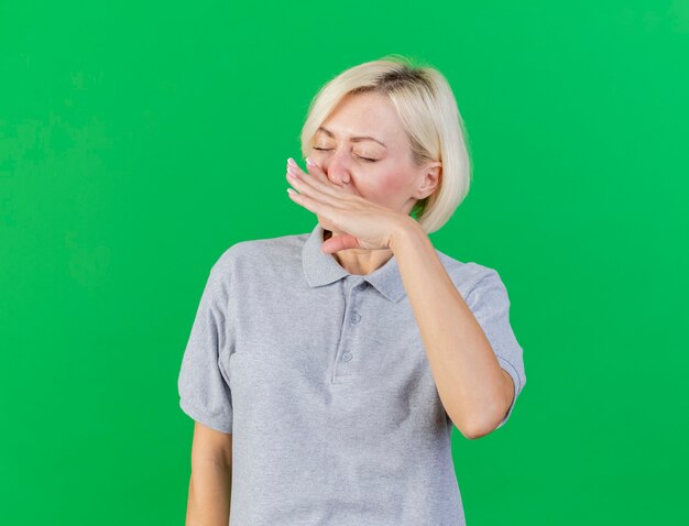Unzufriedene junge blonde kranke slawische Frau wischt Nase mit Hand lokalisiert auf grüner Wand mit Kopienraum ab