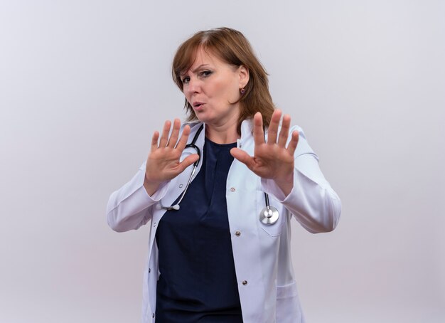 Unzufriedene Ärztin mittleren Alters, die medizinische Robe und Stethoskop trägt, die Stoppgeste auf lokalisiertem weißem Hintergrund mit Kopienraum tun