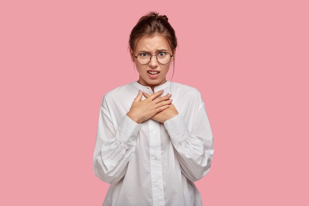 Unzufriedene verärgerte junge Frau mit Brille, die gegen die rosa Wand aufwirft