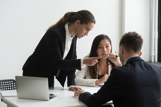 Unzufriedene weibliche Exekutive, die männlichen Angestellten bei der Teambesprechung bedroht