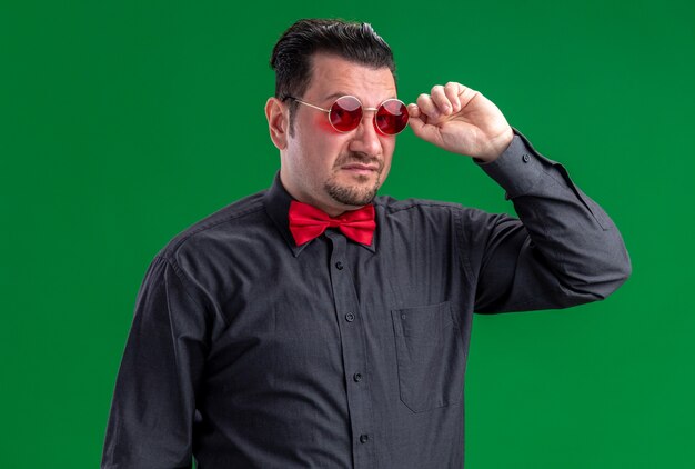 Unzufriedener erwachsener slawischer Mann, der seine rote Sonnenbrille hält und in die Kamera schaut
