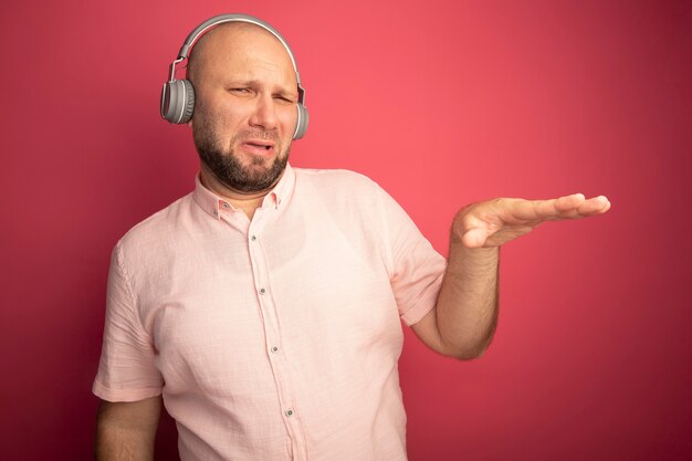 Unzufriedener Glatzkopf mittleren Alters, der rosa T-Shirt und Kopfhörer trägt, die Größe zeigen