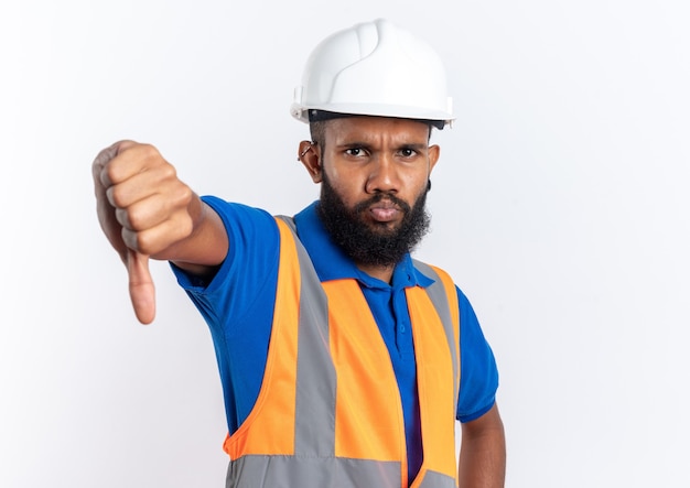 Unzufriedener junger afroamerikanischer baumeister in uniform mit schutzhelm, der isoliert auf weißem hintergrund mit kopienraum herunterdrückt