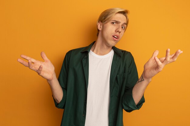 Unzufriedener junger blonder Kerl, der grünes T-Shirt trägt, das Hände ausbreitet