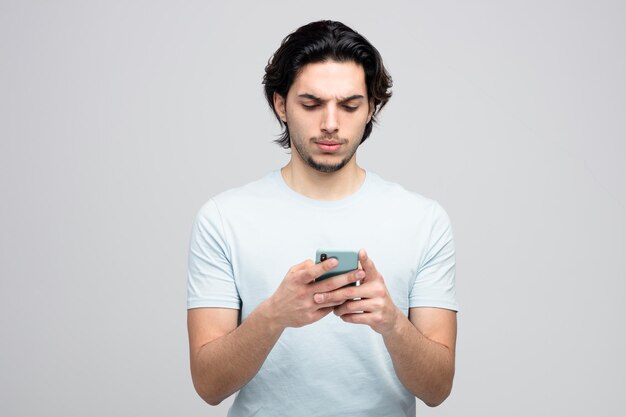 unzufriedener junger gutaussehender Mann mit seinem Handy isoliert auf weißem Hintergrund