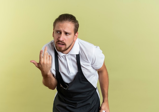 Kostenloses Foto unzufriedener junger hübscher friseur, der seite betrachtet, die hand auf luft lokalisiert auf olivgrünem hintergrund mit kopienraum hält