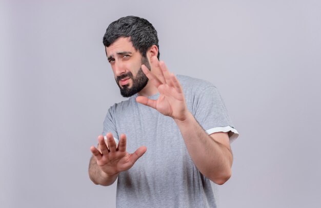 Unzufriedener junger hübscher kaukasischer Mann, der seine Hände in Richtung Kamera ausstreckt, die nicht isoliert auf weißem Hintergrund mit Kopienraum gestikuliert