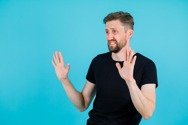 Unzufriedener junger Mann zeigt Stoppgeste, indem er seine Handvoll auf blauem Hintergrund erhebt