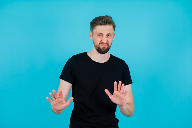 Unzufriedener junger Mann zeigt Stoppgeste mit den Händen auf blauem Hintergrund