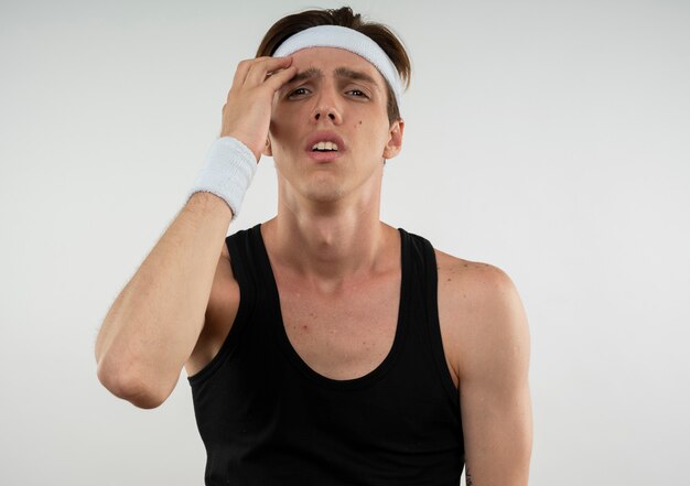 Unzufriedener junger sportlicher Kerl, der Stirnband und Armband trägt Hand auf Stirn lokalisiert auf Weiß