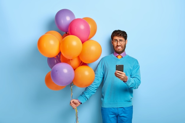 Unzufriedener Kerl mit Luftballons, die im blauen Pullover aufwerfen