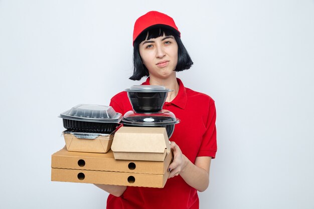 Unzufriedenes junges kaukasisches Liefermädchen, das Lebensmittelbehälter und Verpackungen auf Pizzakartons hält