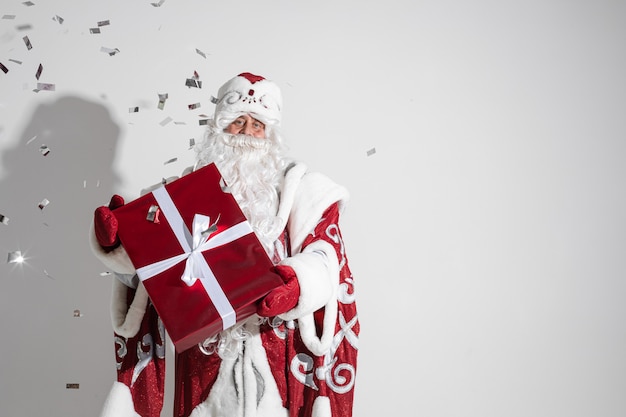 Väterchen Frost in langen warmen Mantel, roten Fäustlingen und einem Hut hält ein Weihnachtsgeschenk mit viel Konfett...