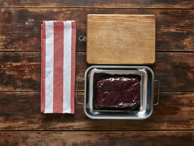 Vakuumverpackung von Walfleischsteak-Metalltopf mit Handtuch und Holzplatte, Draufsicht