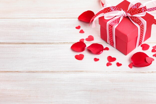 Valentine Geschenk-Box und Rosenblätter auf dem weißen Holzbrett