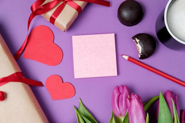 Valentine Hintergrund mit Geschenkbox süße Herzen und Tulpen auf violettem Tisch Draufsicht flach liegen